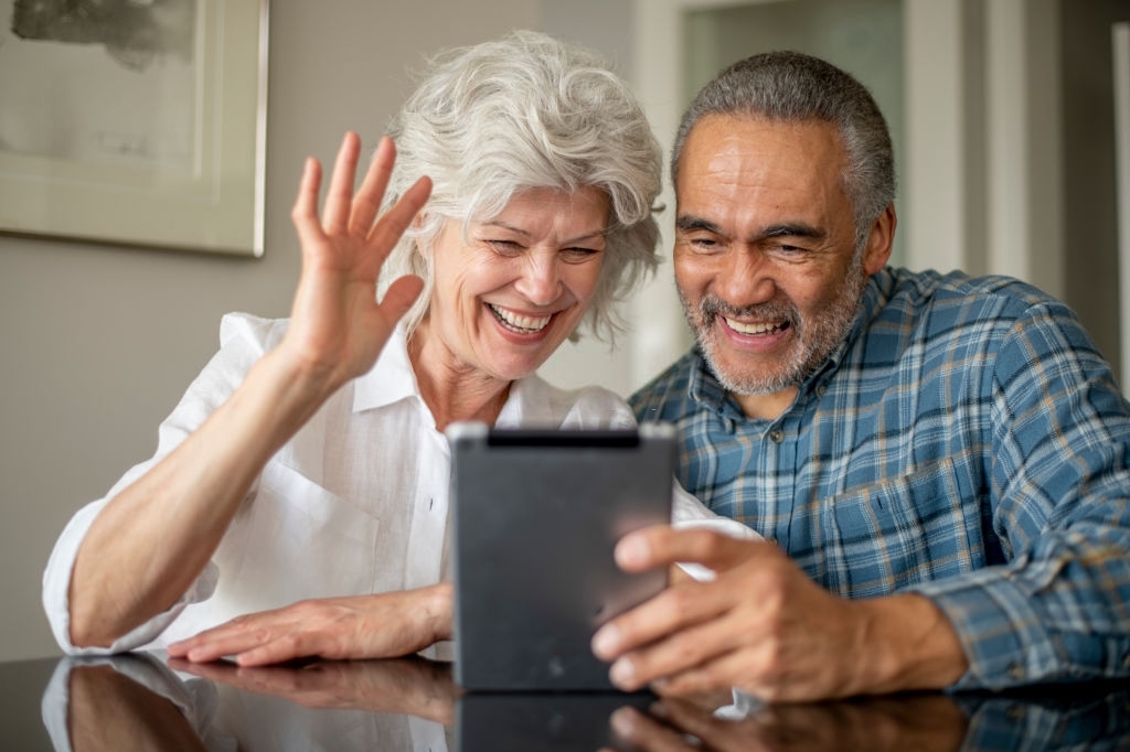 Married senior couple talks with friends through video chat.