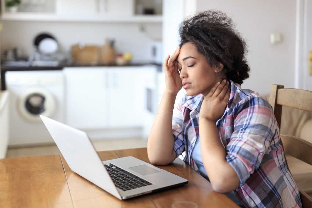 Young woman working at home, using laptop, having headache.